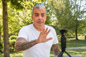 56-jähriger Mann macht ein Handzeichen vor einer Pocket-Kamera und schaut überrascht